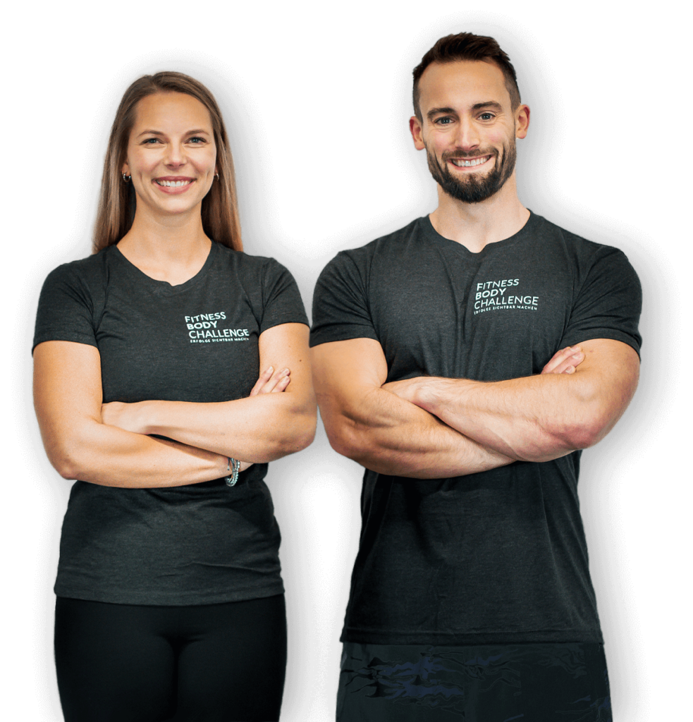 Janice und Jan in dunkelgrauen T-Shirts mit dem Logo "Fitness Body Challenge" stehen nebeneinander. Die Coaches hinter der Fitness Body Challenge lächeln und haben die Arme verschränkt. Jan hat einen Bart und kurze dunkle Haare, Janice hat langes blondes Haar.